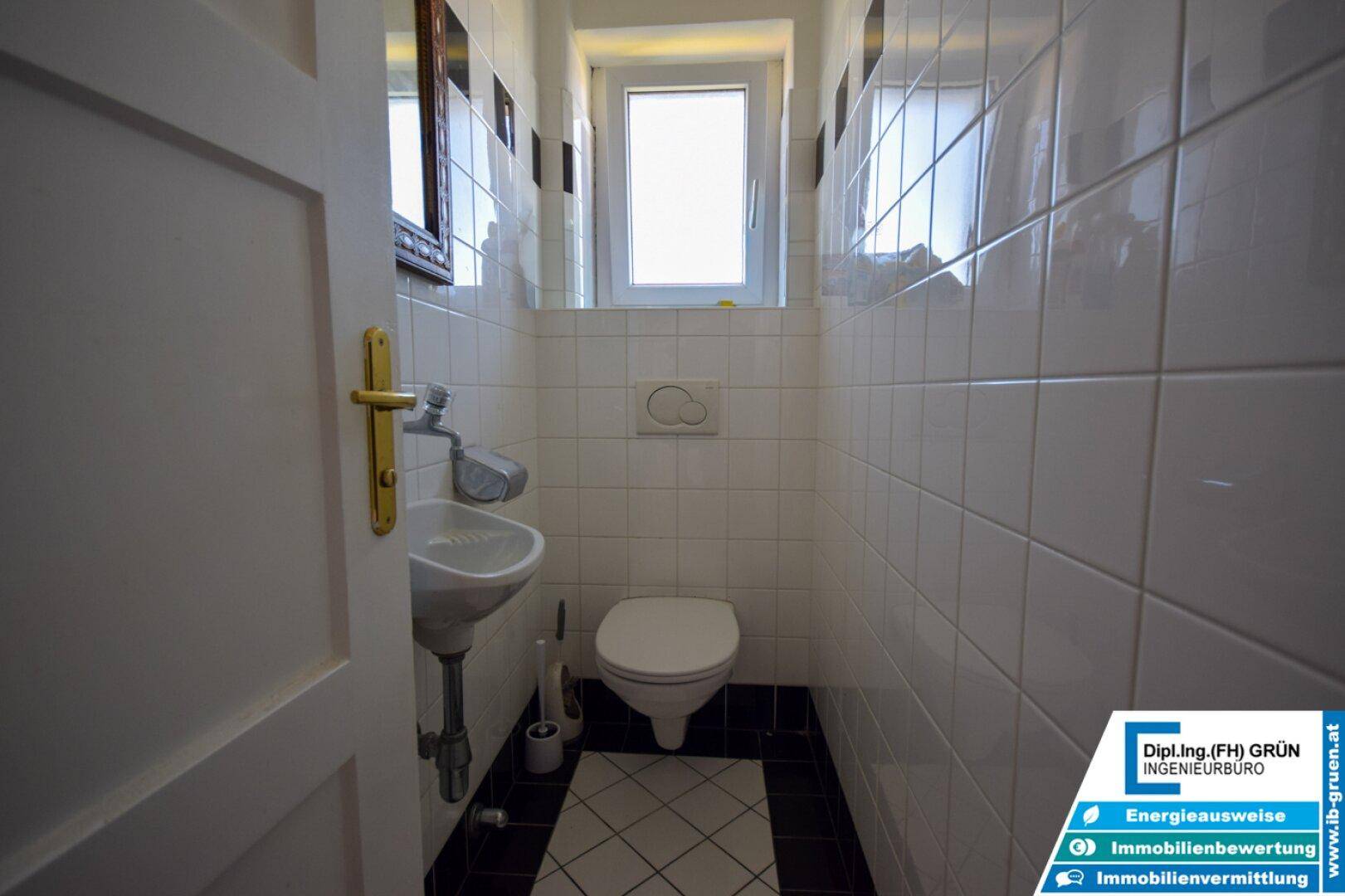 Kleines Gäste-WC mit weißer Fliesenwand, Fenster und modernem Waschbecken.