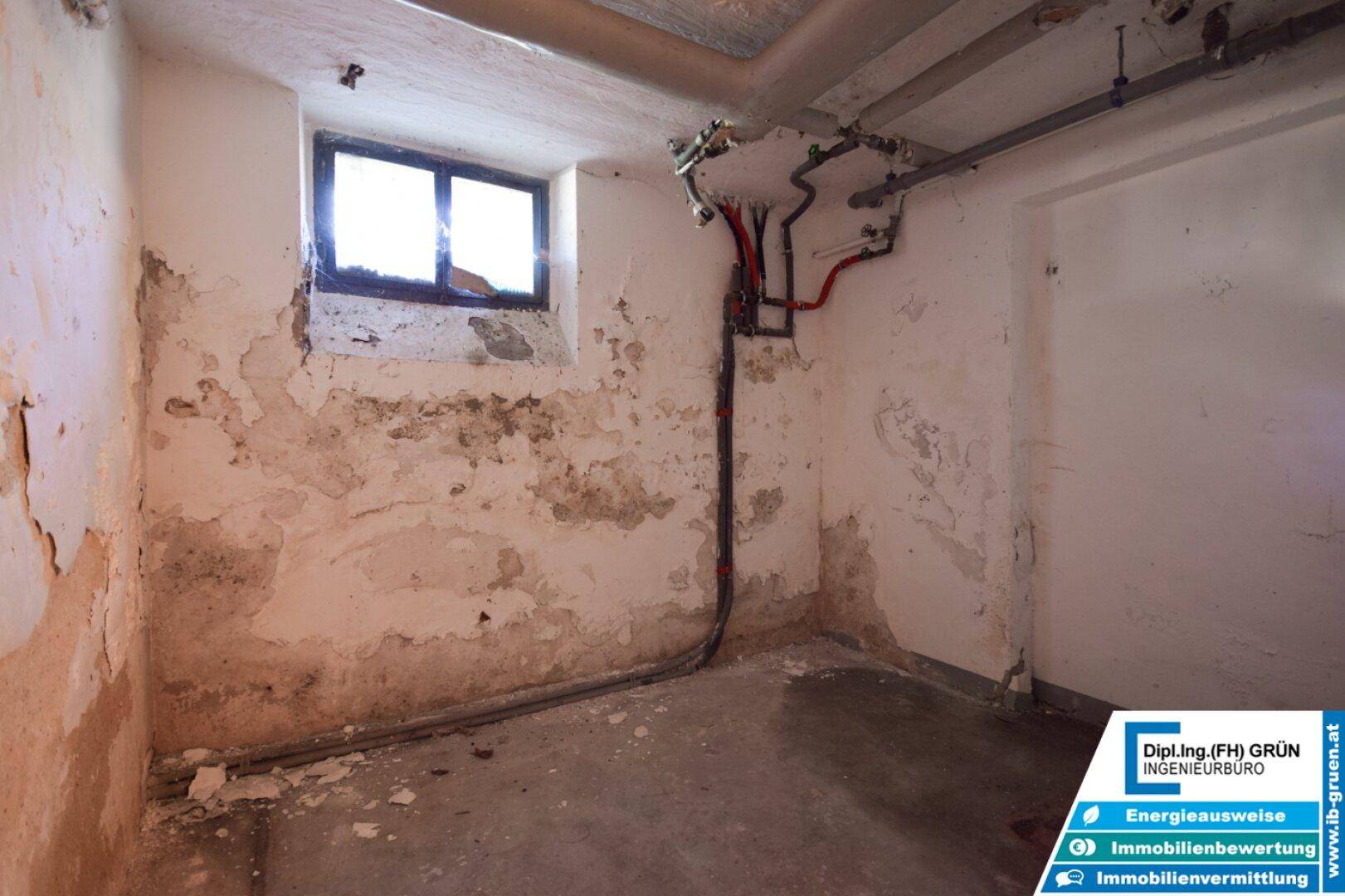 Kellerraum mit unverputzten Wänden, sichtbaren Rohren und einem kleinen Fenster.