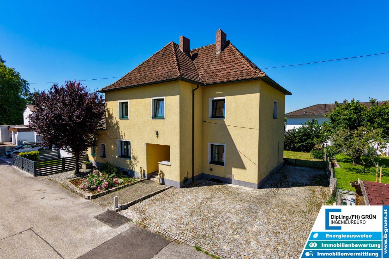 Freistehendes Haus mit gelber Fassade, gepflasterter Einfahrt und Vorgarten.