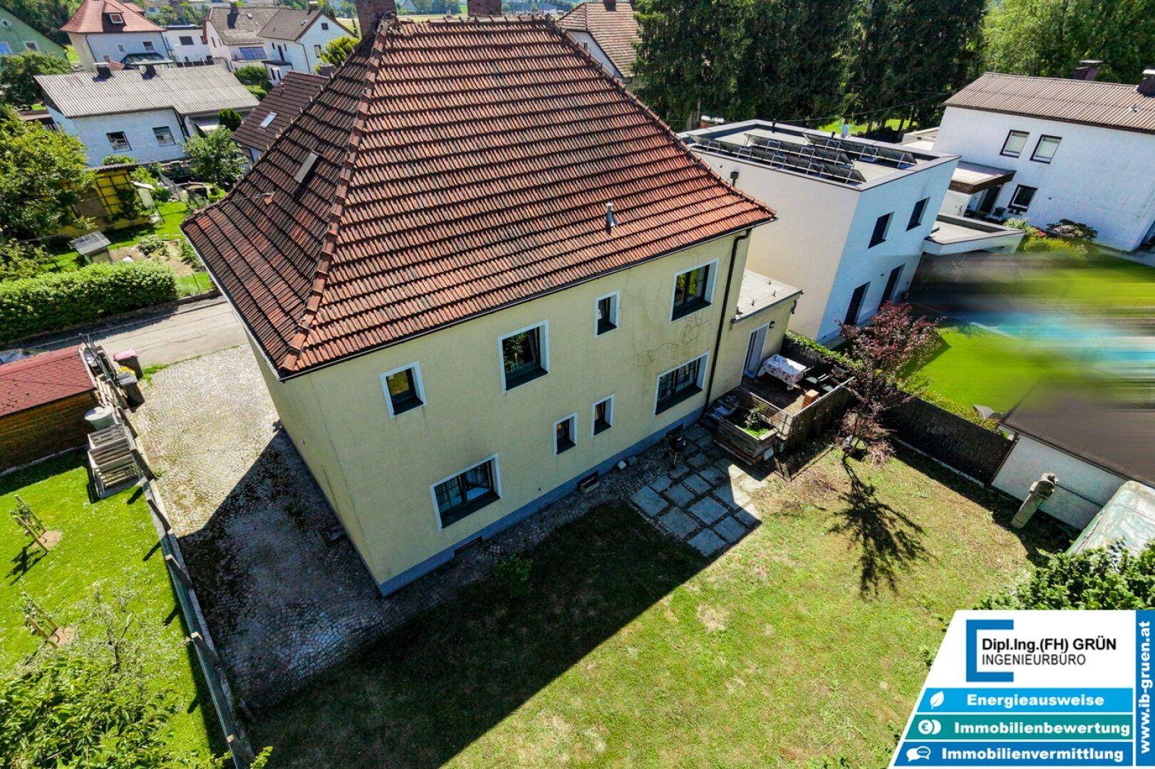 Luftaufnahme des Hauses von hinten mit großem Garten, Rasen und gepflastertem Bereich.
