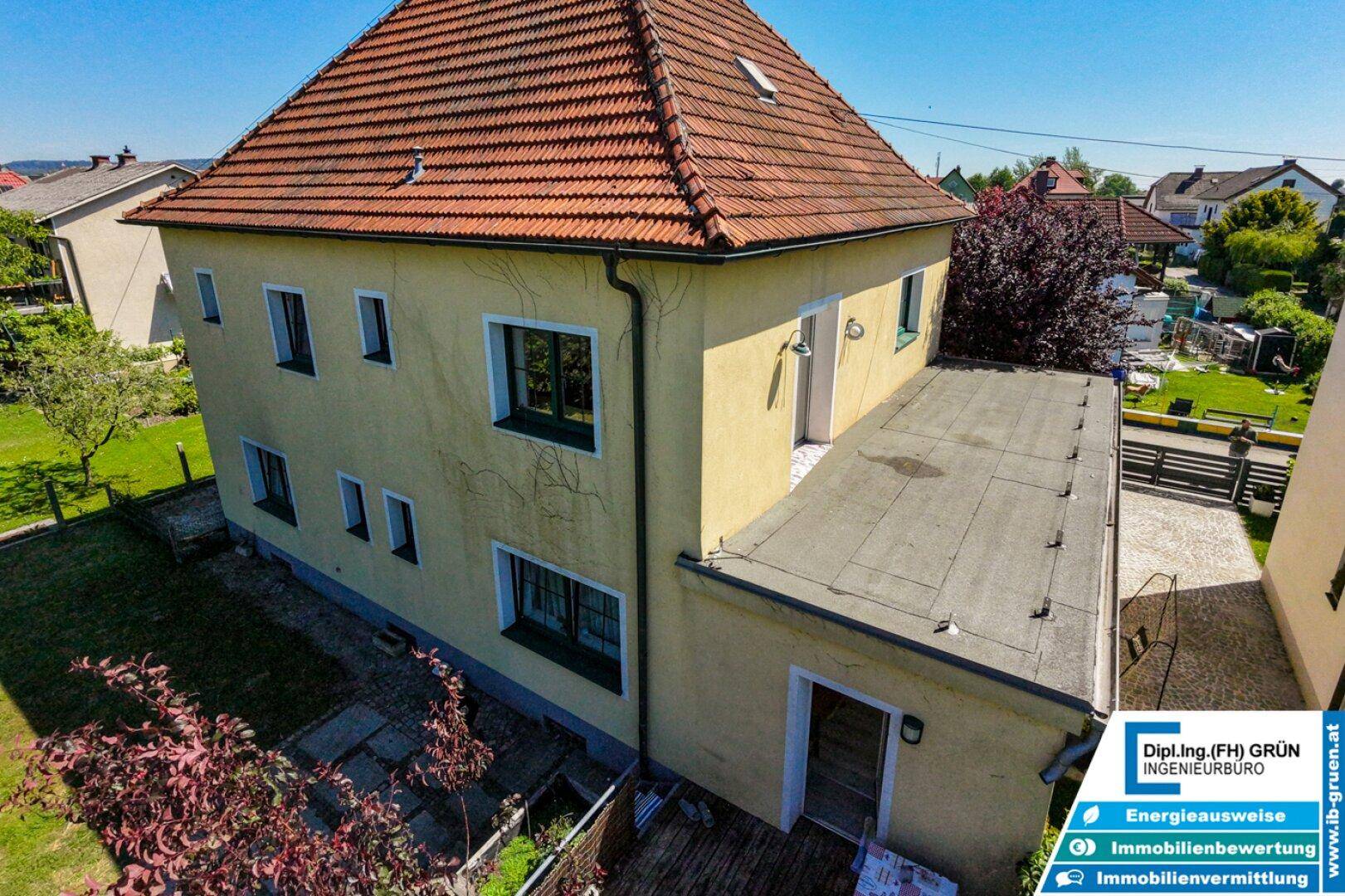 Seitenansicht des Hauses mit gelber Fassade, Flachdachanbau und Gartenbereich.