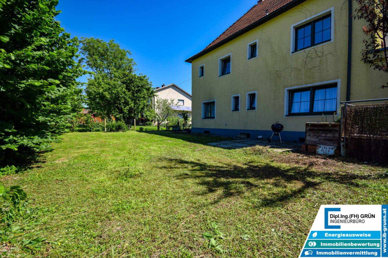 Weitläufiger grüner Garten neben dem gelben Haus mit Grillplatz und viel Sonnenlicht.