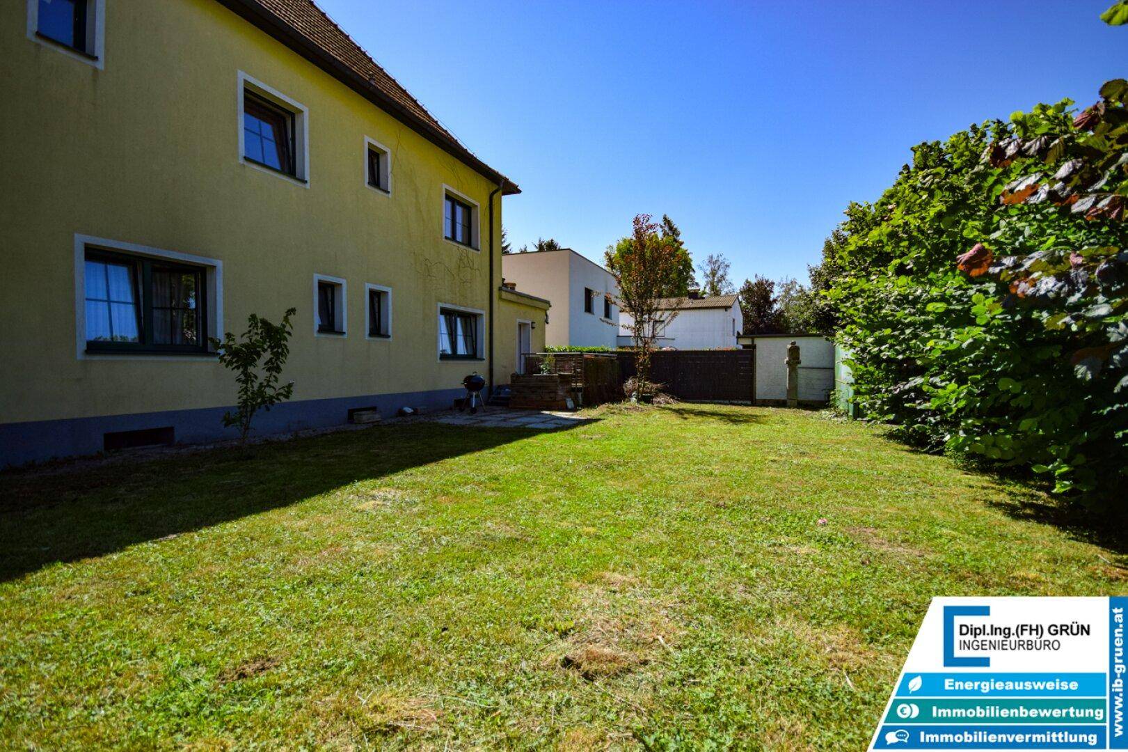 Großer, gepflegter Gartenbereich mit Rasenfläche und Hecke hinter dem gelben Wohnhaus.