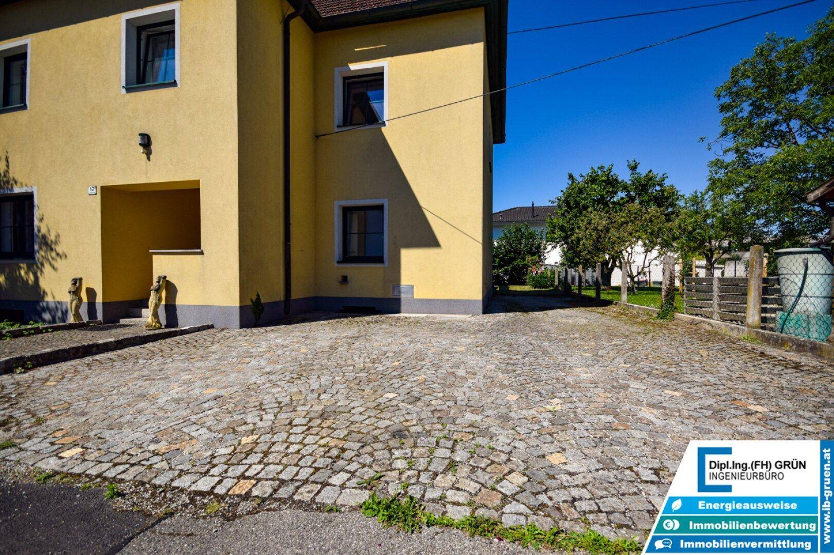 Geräumige gepflasterte Parkfläche vor dem gelben Haus, bietet Platz für mehrere Fahrzeuge.