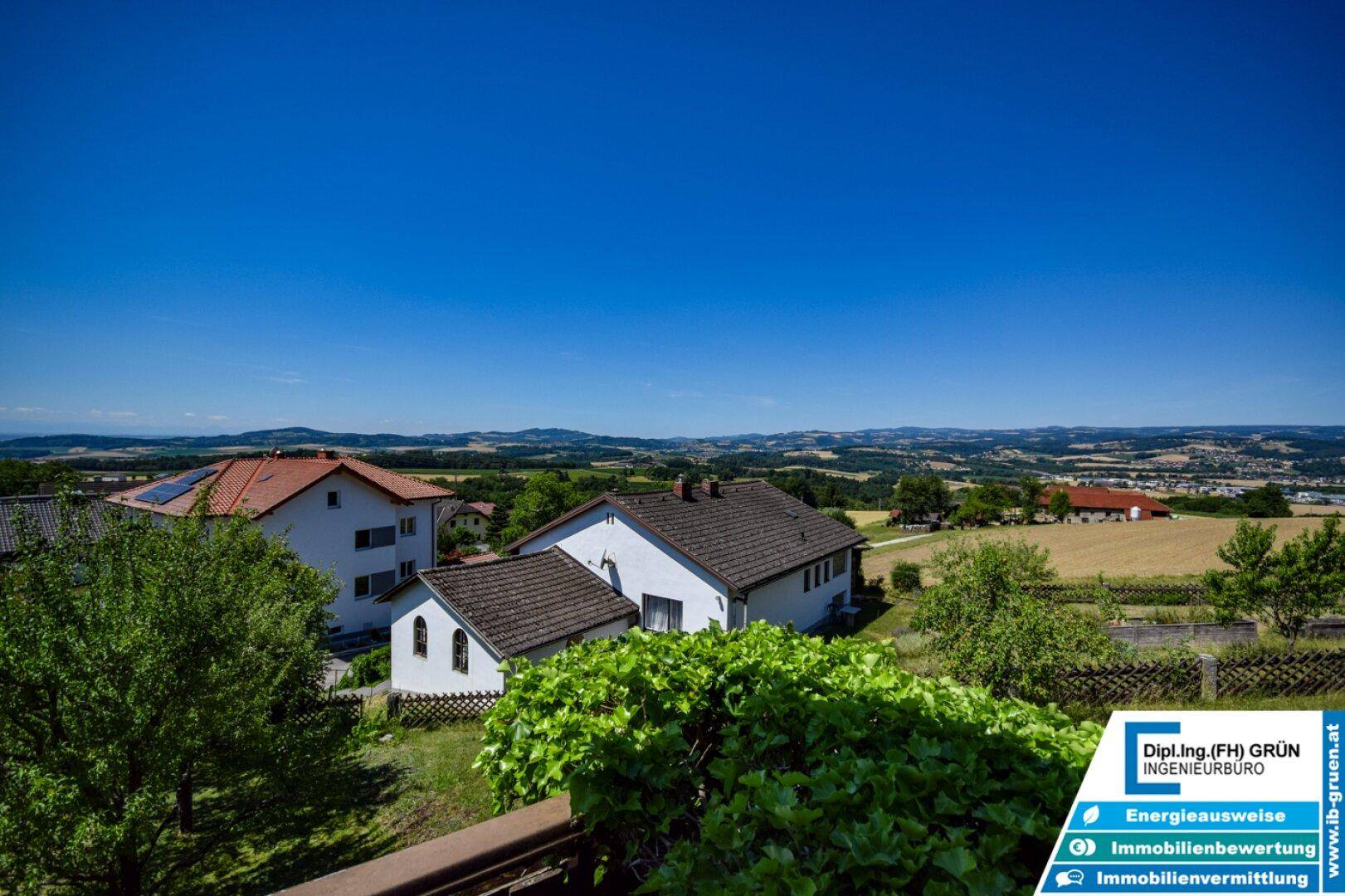 Panoramablick über die hügelige Landschaft und benachbarte Häuser unter blauem Himmel.
