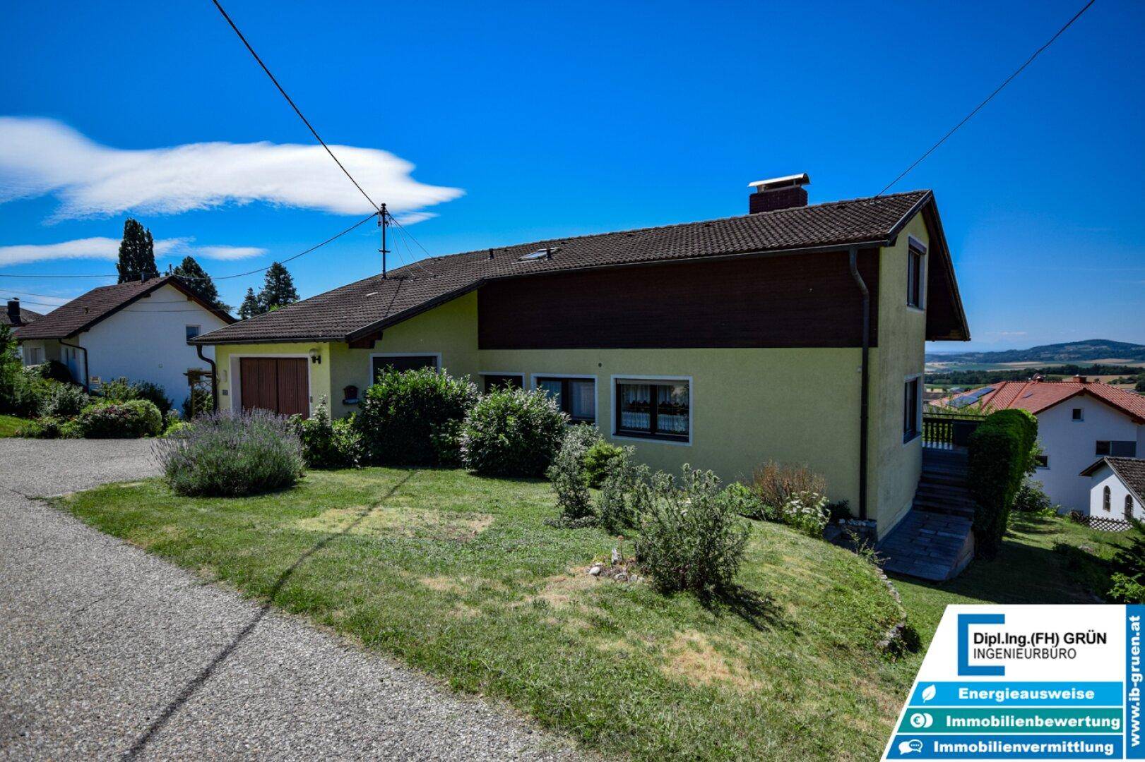 Seitenansicht des Hauses mit Vorgarten und Zufahrt unter blauem Himmel.