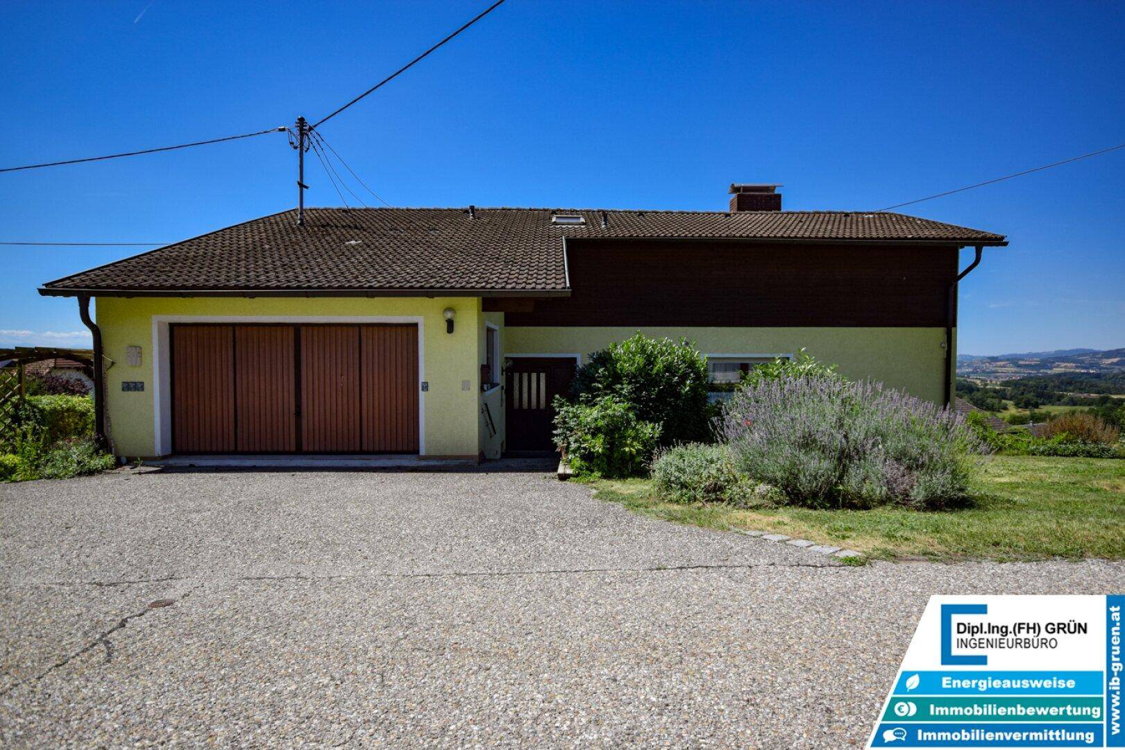 Vorderansicht des Hauses mit Garage und gepflasterter Einfahrt unter blauem Himmel.