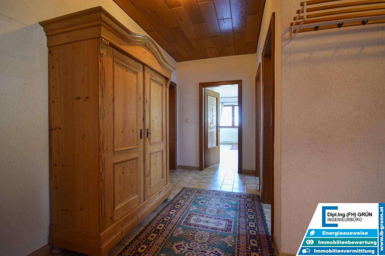 Heller Flur mit Holzschrank, Teppich und Zugang zu weiteren Räumen.