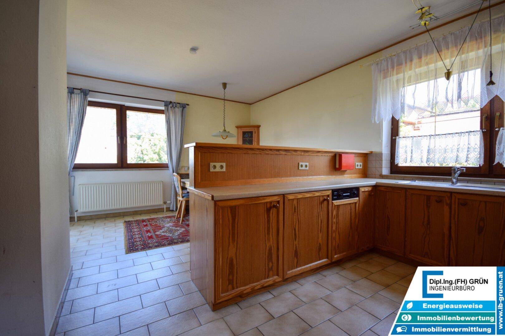 Traditionelle Küche mit Holzschränken, Fliesenboden und Essbereich am Fenster.