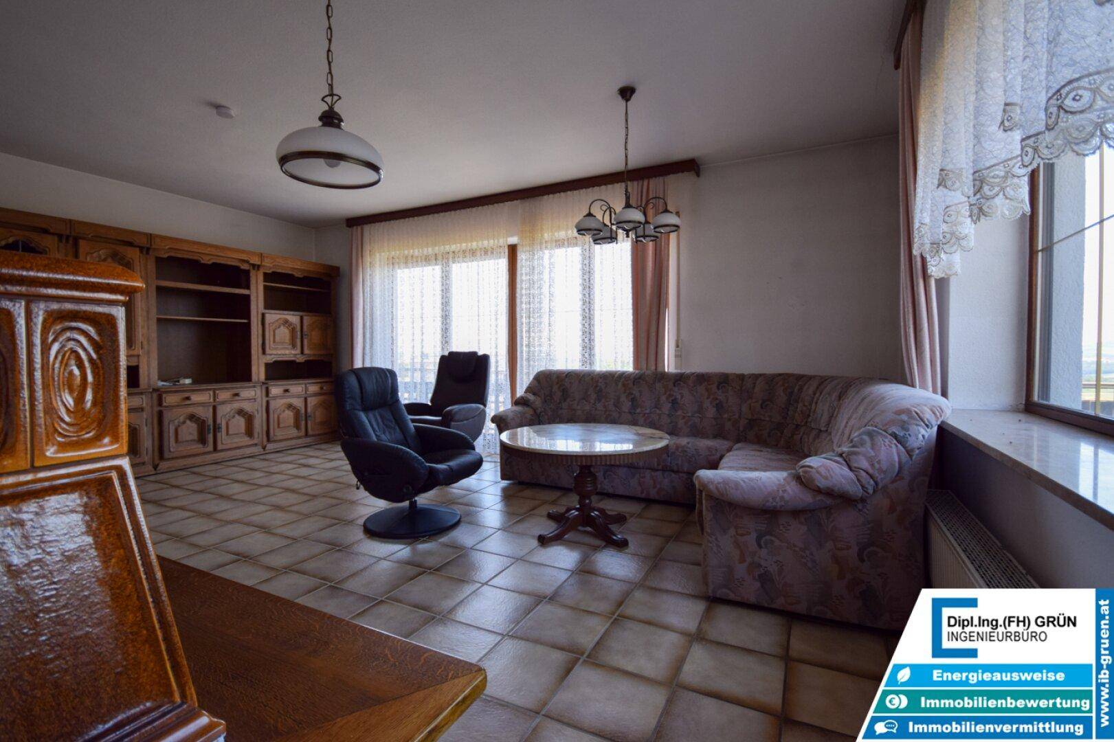 Geräumiges Wohnzimmer mit Fliesenboden, traditionellen Möbeln und großen Fenstern.