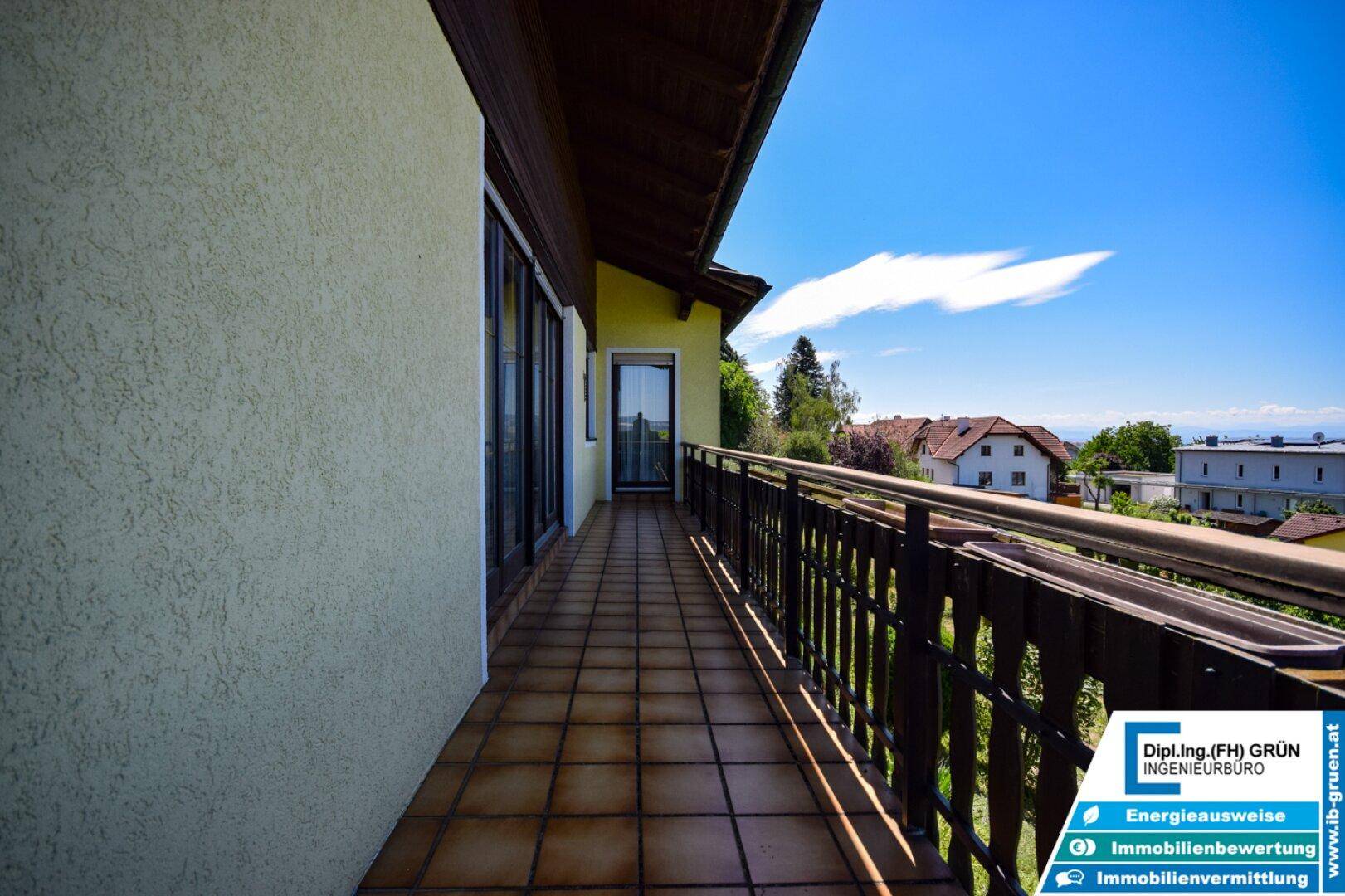 Langer Balkon mit Fliesenboden und Holzgeländer, bietet einen weiten Blick in die Landschaft.