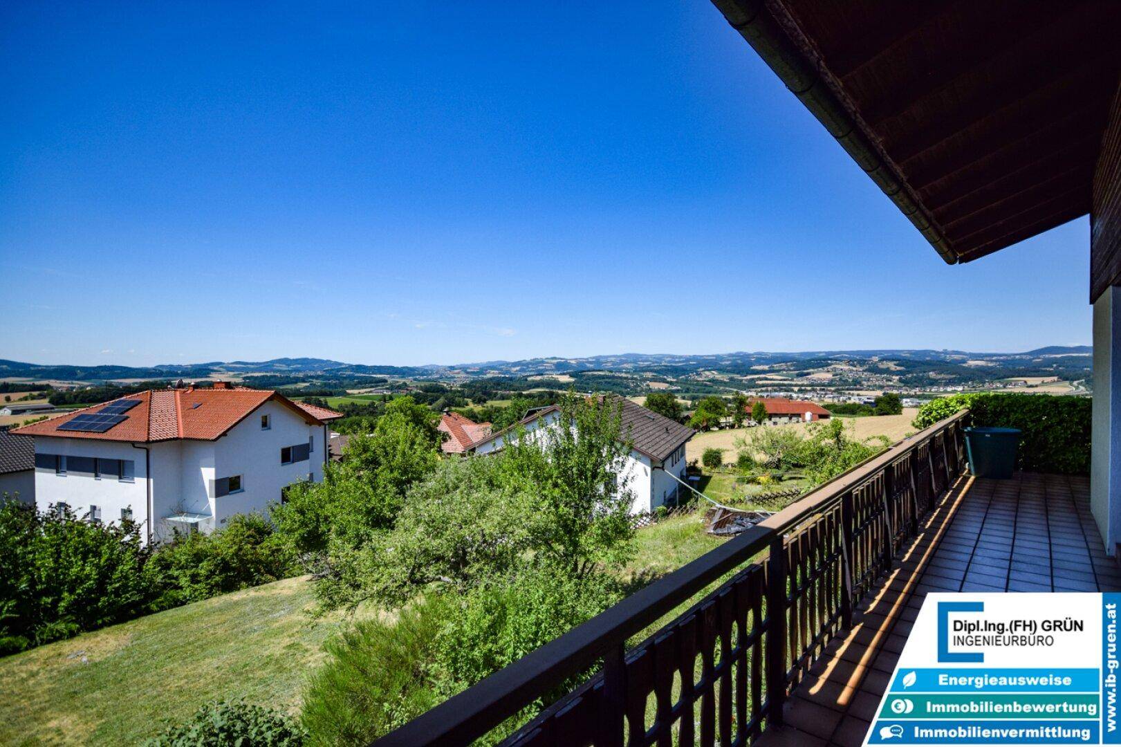 Geräumiger Balkon mit weitem Blick über die grüne Hügellandschaft und umliegende Häuser.