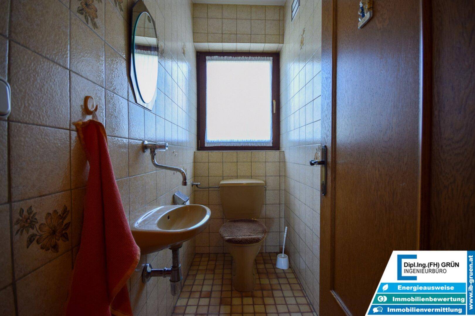 Kleines Gäste-WC mit beigefarbenen Fliesen, Fenster und einfacher Ausstattung.