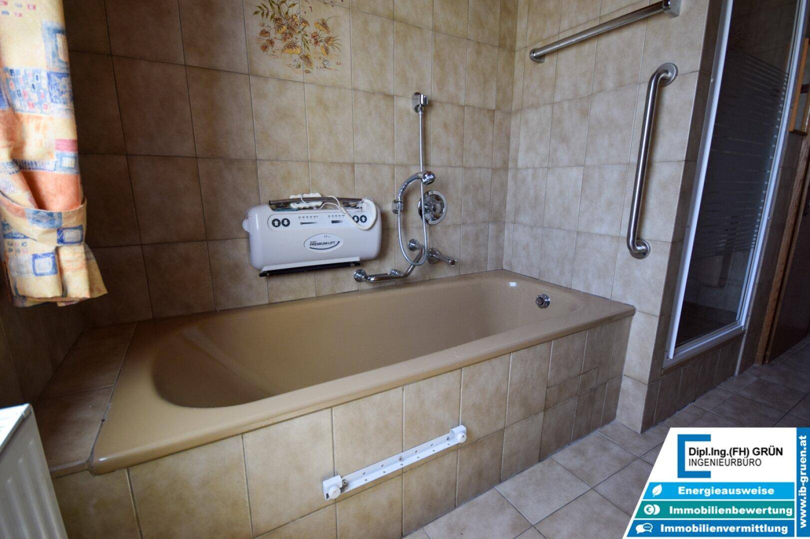 Badewanne mit Duscharmatur und Haltegriffen in einem gefliesten Badezimmer.