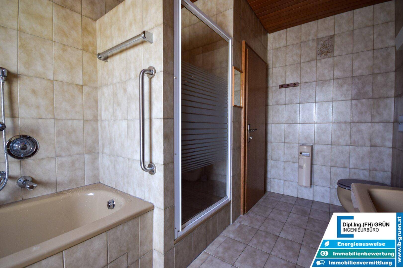 Badezimmer mit Duschkabine, Badewanne und WC, alles in beigefarbenen Fliesen gehalten.