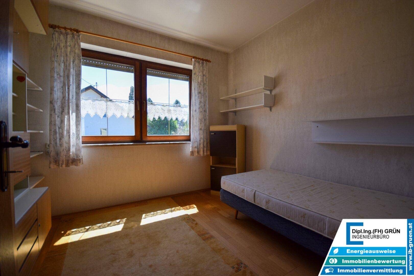 Helles Schlafzimmer mit Einzelbett, Holzfußboden und großem Fenster.