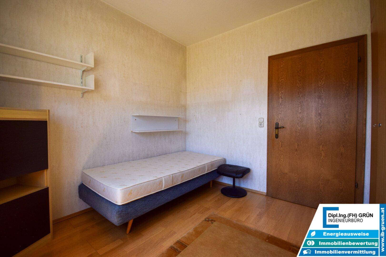 Schlafzimmer mit Einzelbett, Holzfußboden und schlichten Regalen an der Wand.