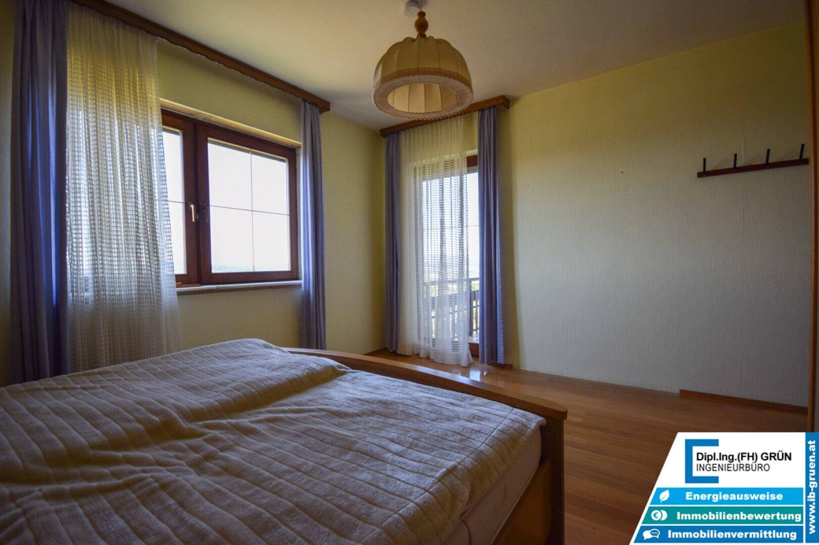 Schlafzimmer mit Doppelbett und Zugang zu einem Balkon, bietet viel Tageslicht.
