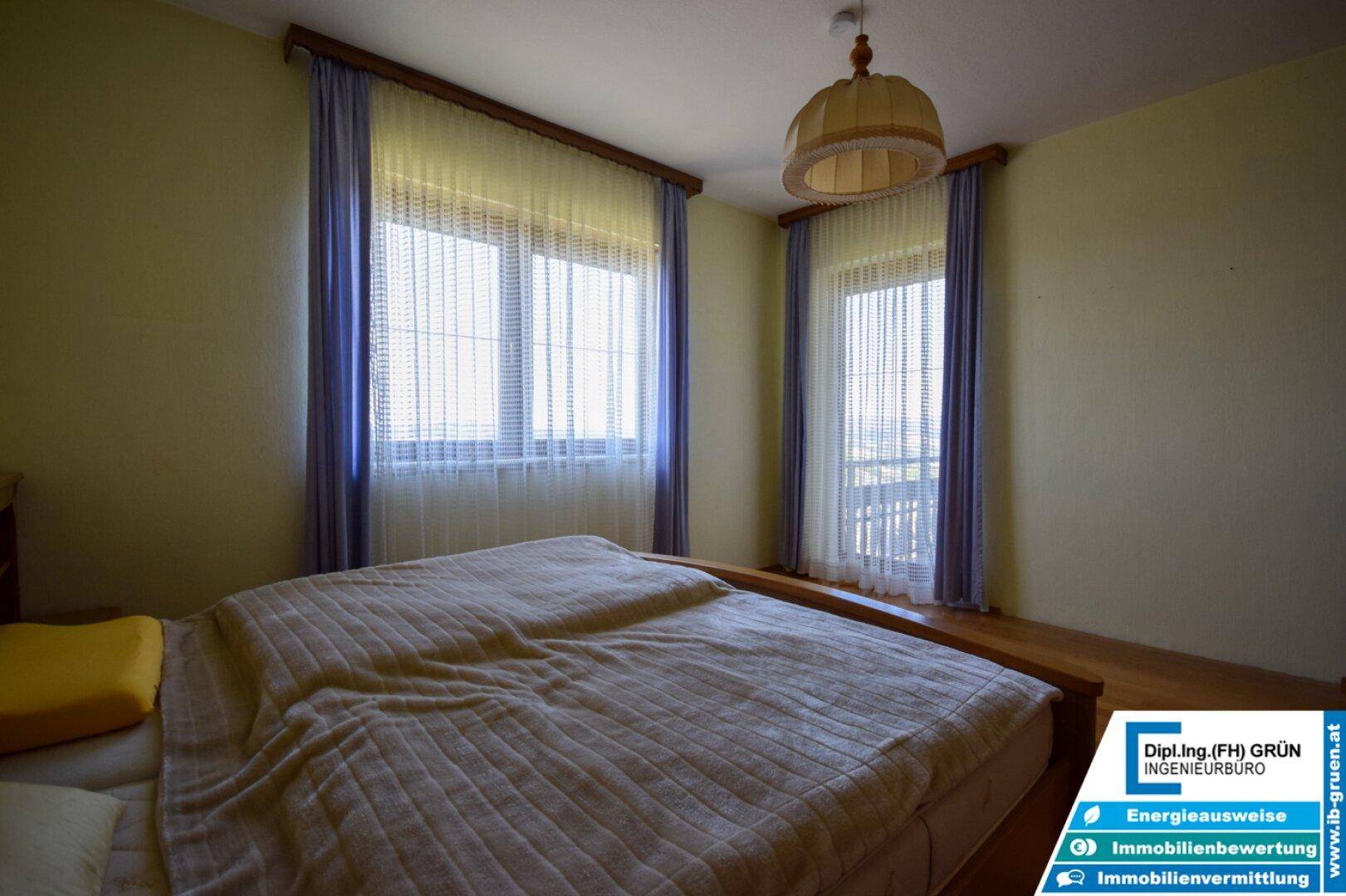 Helles Schlafzimmer mit Doppelbett und zwei Fenstern, die viel Licht hereinlassen.