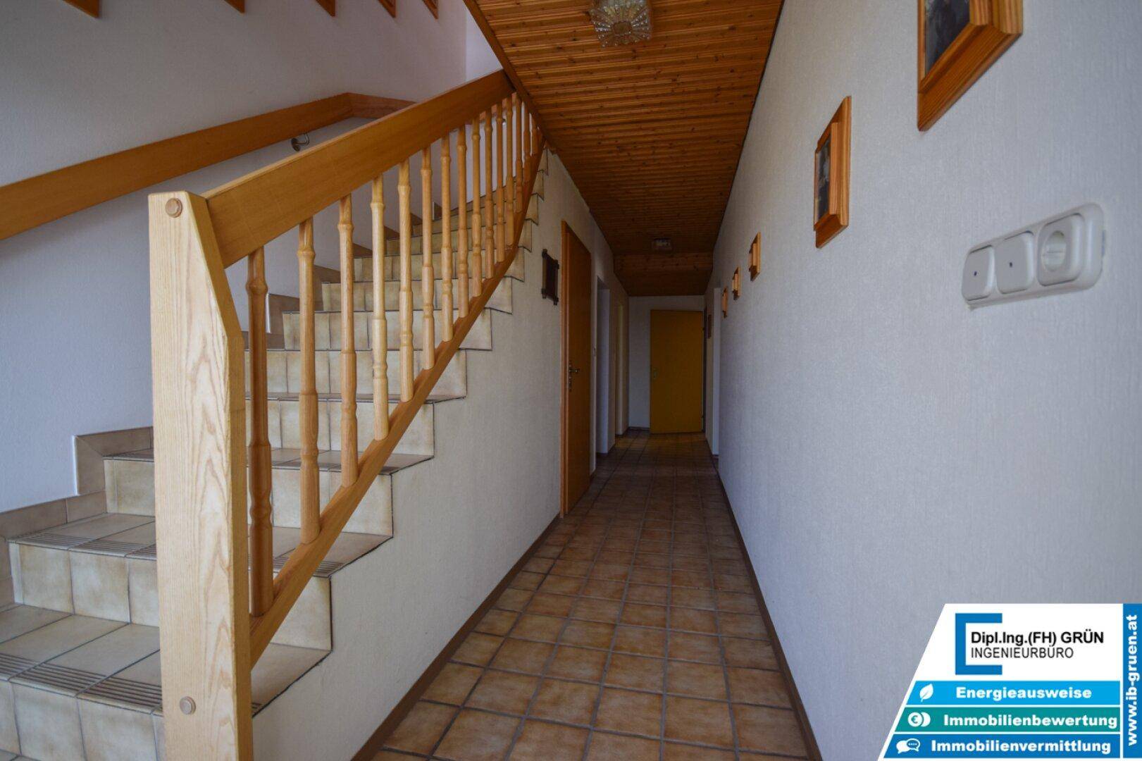 Langer Flur mit Holztreppe und Fliesenboden, verbindet die Räume im Obergeschoss.