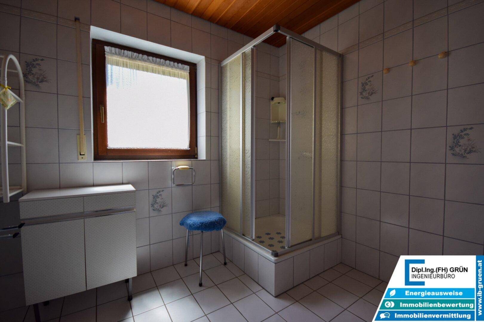 Badezimmer mit Duschkabine, Fenster und gefliesten Wänden im Retro-Stil.