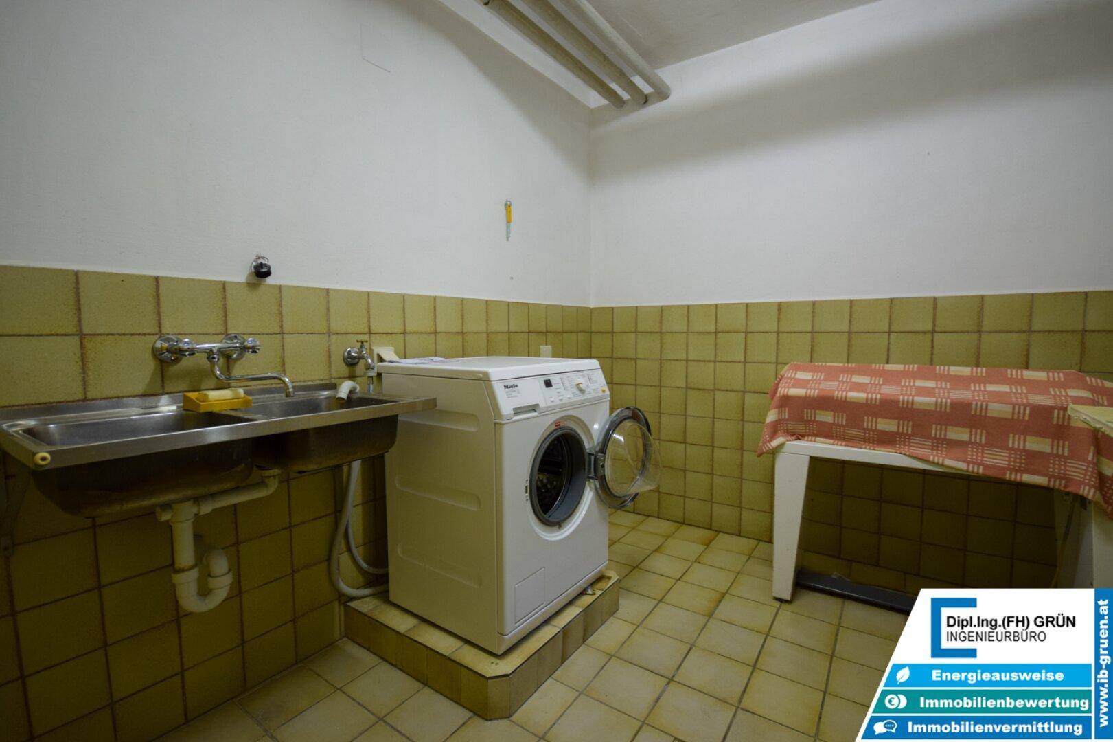 Praktischer Waschraum mit Waschmaschine, Spülbecken und gefliesten Wänden.