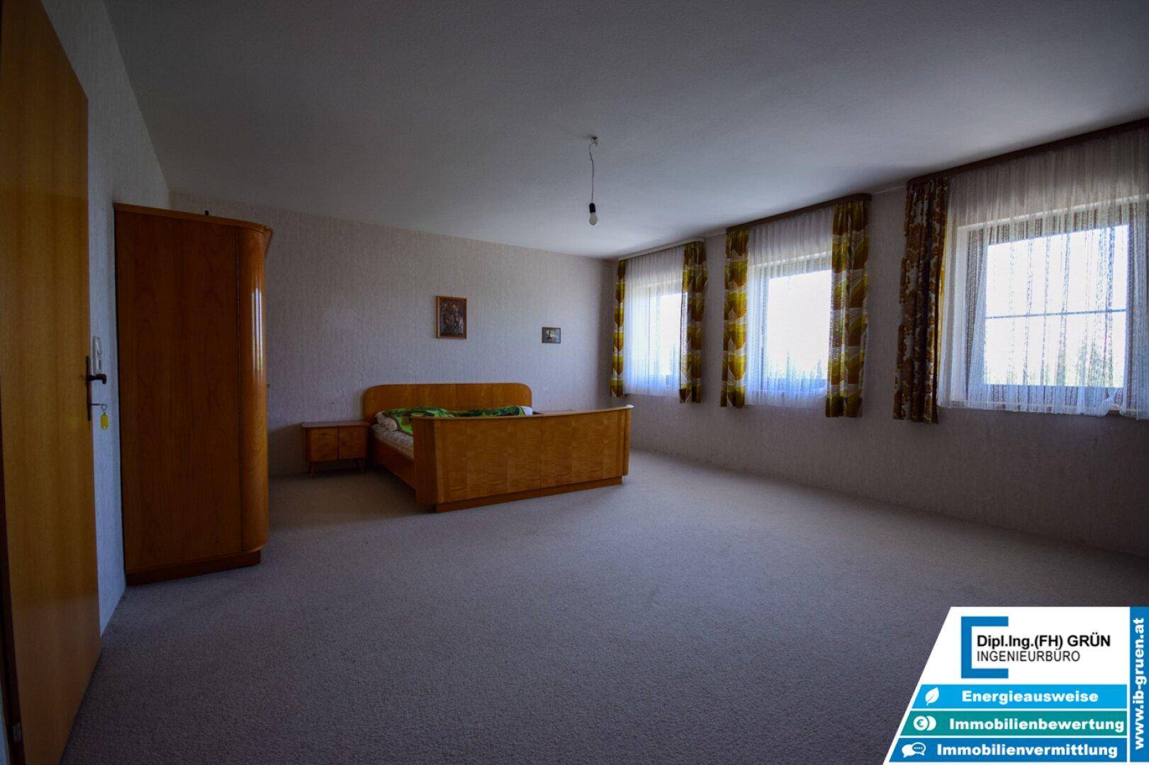 Geräumiges Schlafzimmer mit Teppichboden, Holzmöbeln und vielen Fenstern.