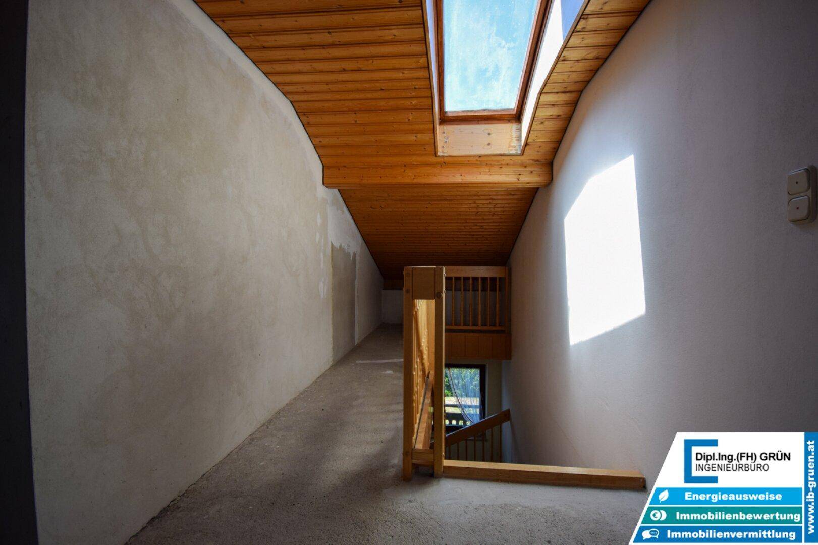 Dachbodenbereich mit Holzdecke, Dachfenster und Blick auf die Treppe.