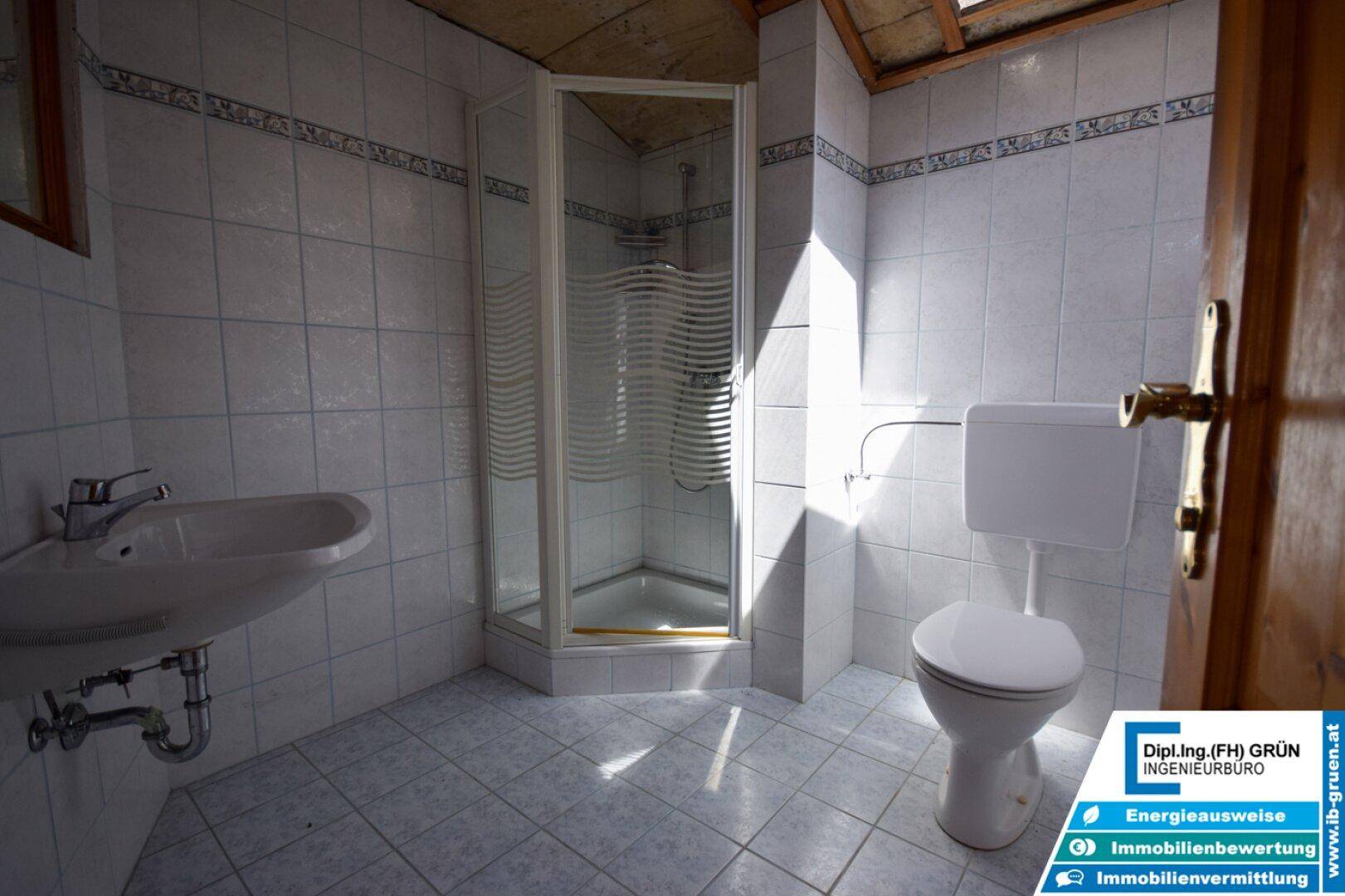Einfaches Badezimmer mit Dusche, WC und Waschbecken, gefliest in hellen, funktionalen Farben.