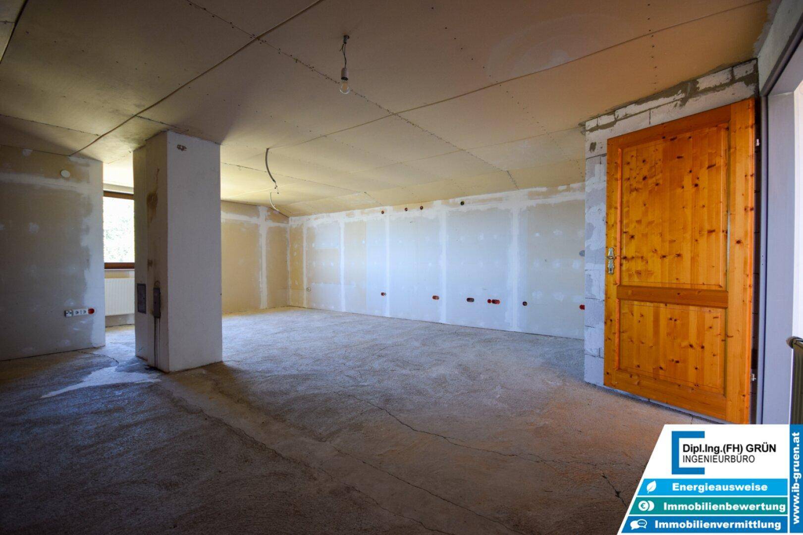 Großer Rohbau-Raum mit Holztür und Fenster, wartet auf den Innenausbau und die Fertigstellung.