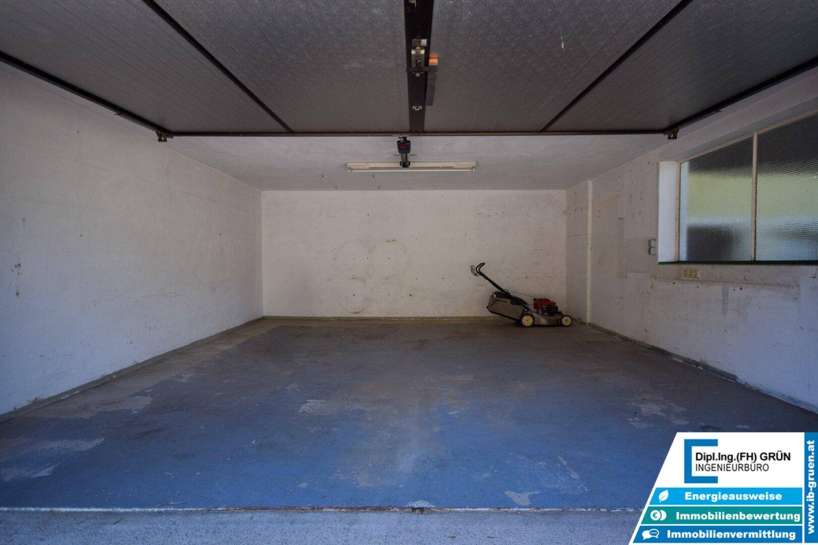 Geräumige Garage mit Betonboden und Rasenmäher, bietet viel Stauraum und Arbeitsfläche.