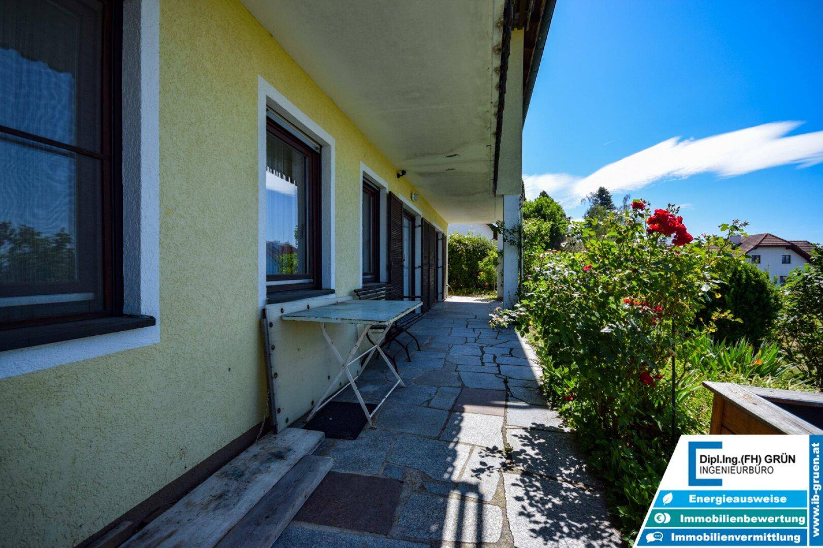 Terrasse mit Steinfliesen und Blumenbeeten entlang der Hauswand, einladend und gepflegt.