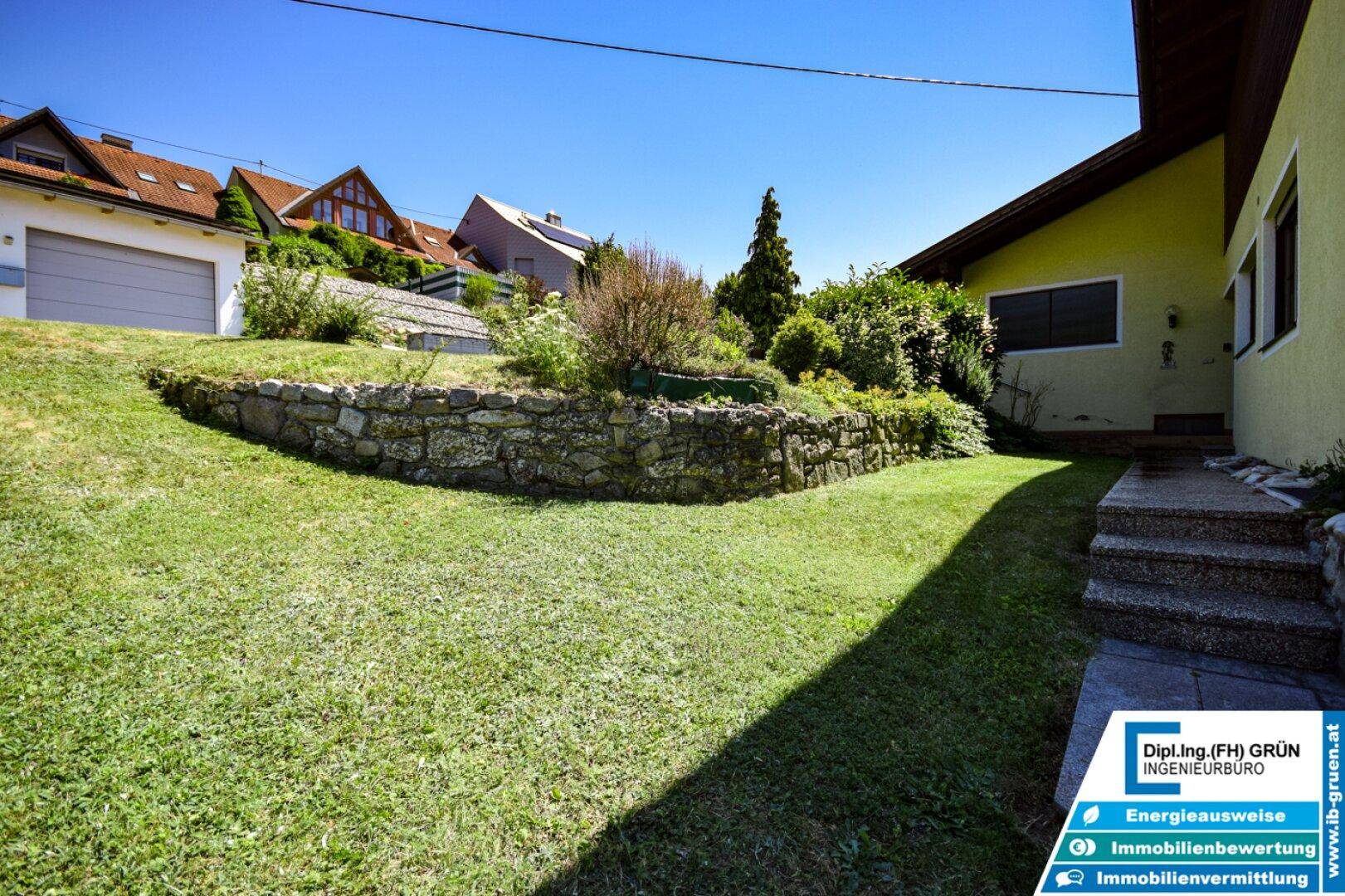 Gepflegter Gartenbereich mit Rasen, Steinmauer und Treppe zum Haus, harmonisch gestaltet.