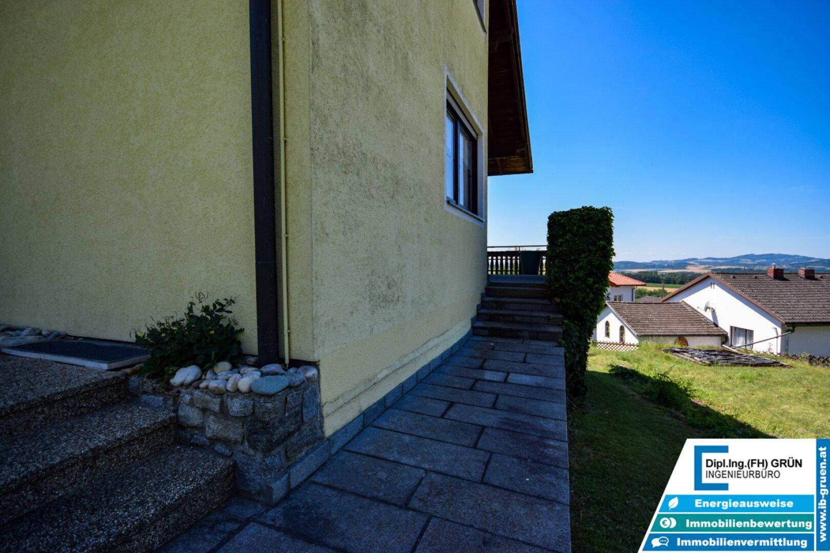 Seitlicher Zugang zum Haus mit Steintreppe und gepflastertem Weg, umgeben von Grün.