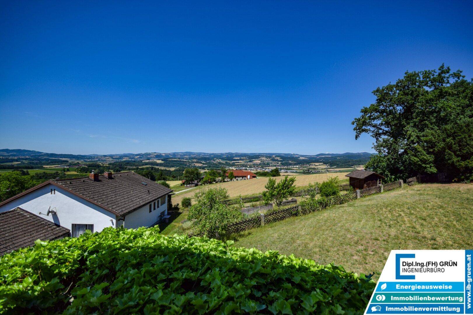 Panoramablick über die hügelige Landschaft mit Feldern und Häusern in der Ferne.