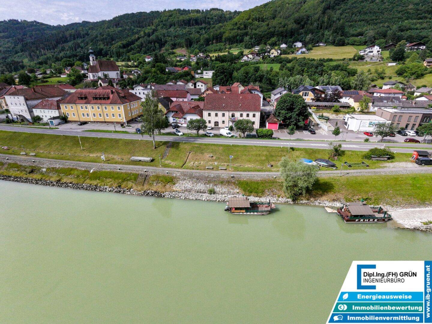 Luftaufnahme des Flusses und des Dorfes mit grünen Hügeln im Hintergrund und Booten am Ufer.