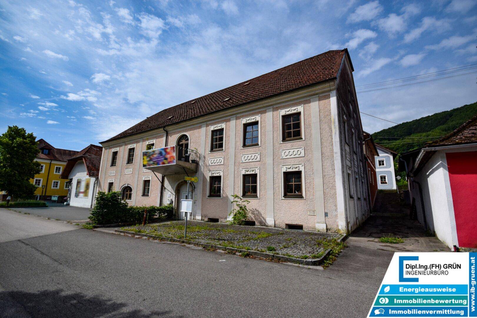 Historisches Gebäude mit rosafarbener Fassade und traditionellen Fenstern an einer ruhigen Straße.