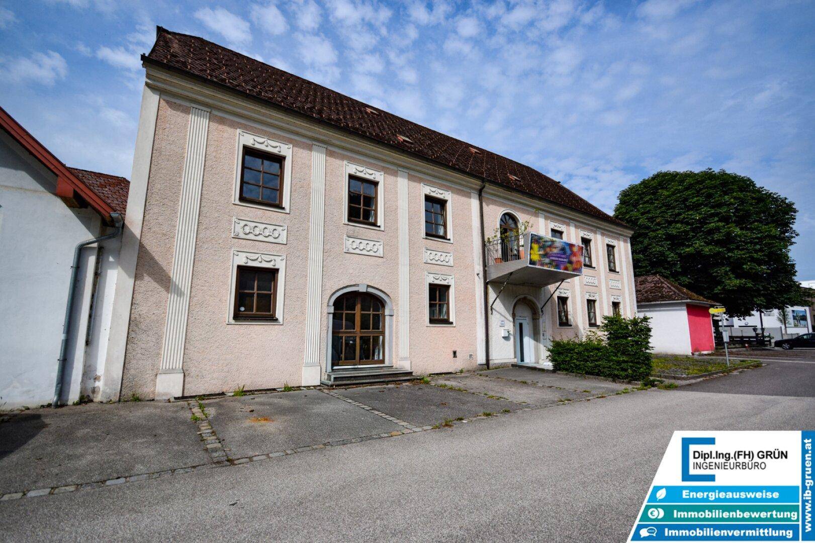 Ansicht der historischen Fassade mit dekorativen Elementen und einem kleinen Balkon unter blauem Himmel.