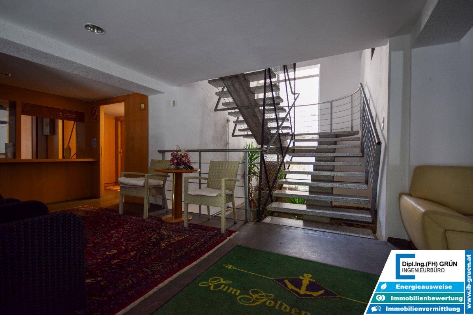 Gemütlicher Empfangsbereich mit Sitzgelegenheiten, Teppichboden und einer offenen Treppe im Hintergrund.