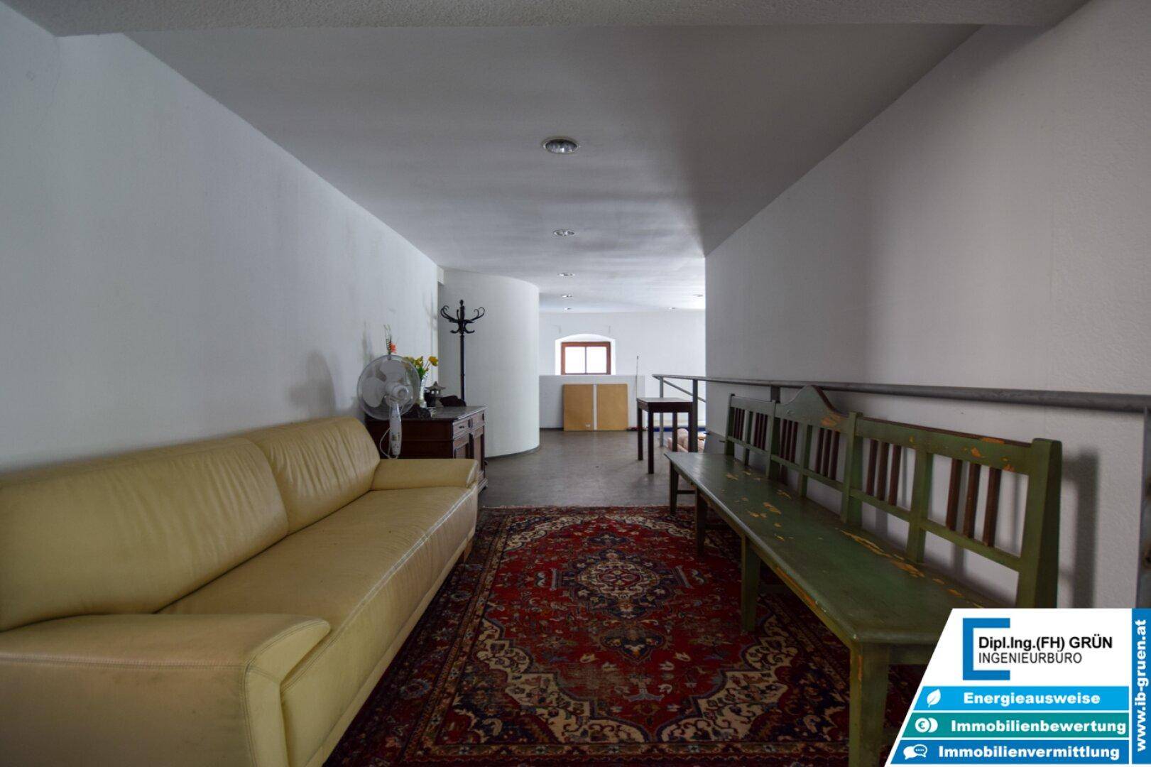 Langer Flur mit beiger Couch, Holzbank und einem traditionellen Teppichboden.