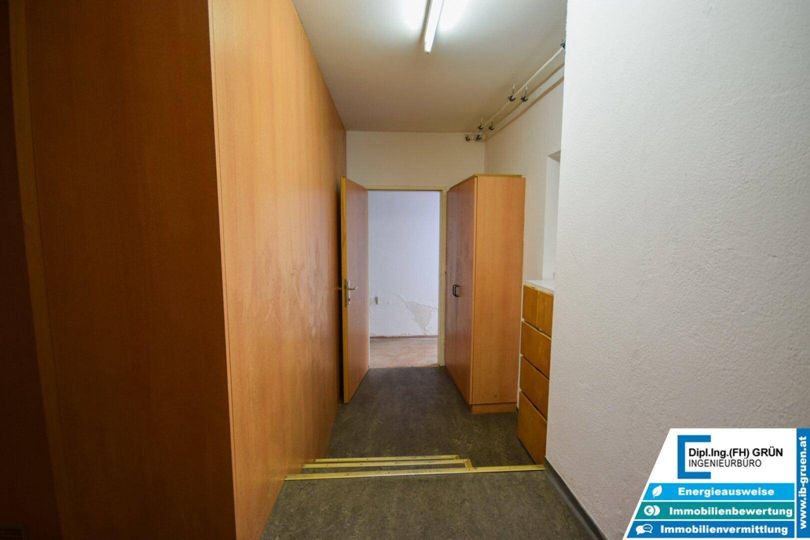 Schmaler Flur mit Holzverkleidung an den Wänden und einer offenen Tür zu einem weiteren Raum.