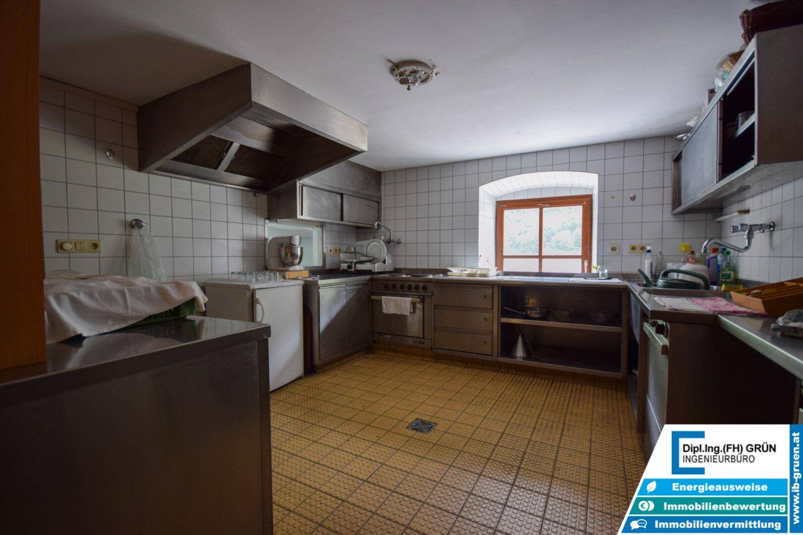 Ältere Küche mit weißen Fliesenwänden, Edelstahlgeräten und einem kleinen Fenster.