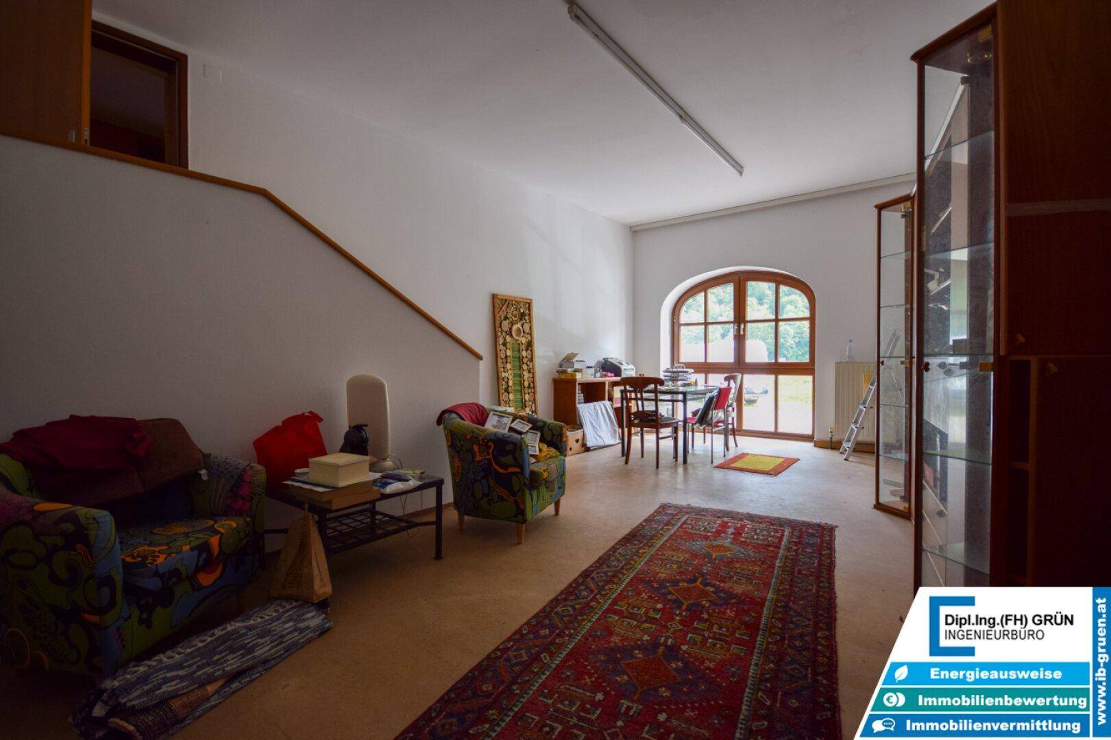 Großer Wohnbereich mit Teppich, verschiedenen Sitzgelegenheiten und einem Rundbogenfenster.