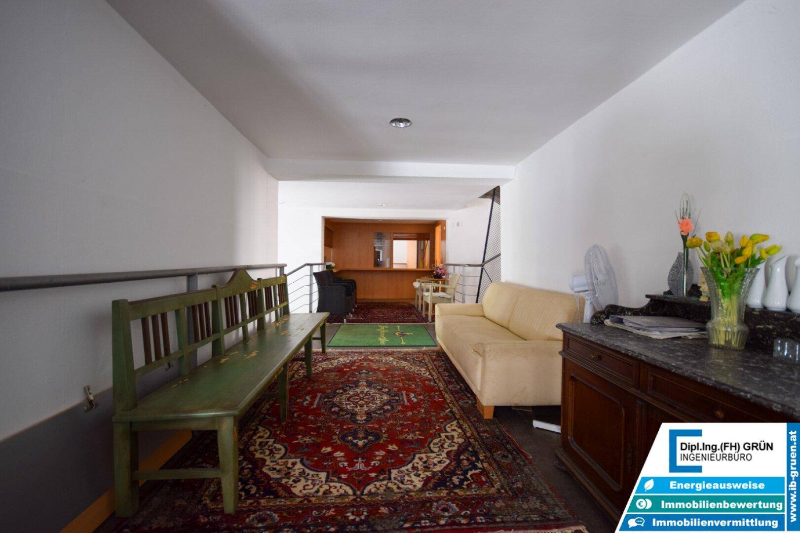 Langer Flur mit beiger Couch, Holzbank und einem traditionellen Teppichboden.