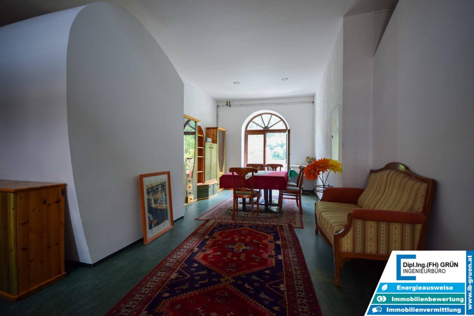 Langer Flur mit Sitzgelegenheiten, Teppich und einem großen Rundbogenfenster.