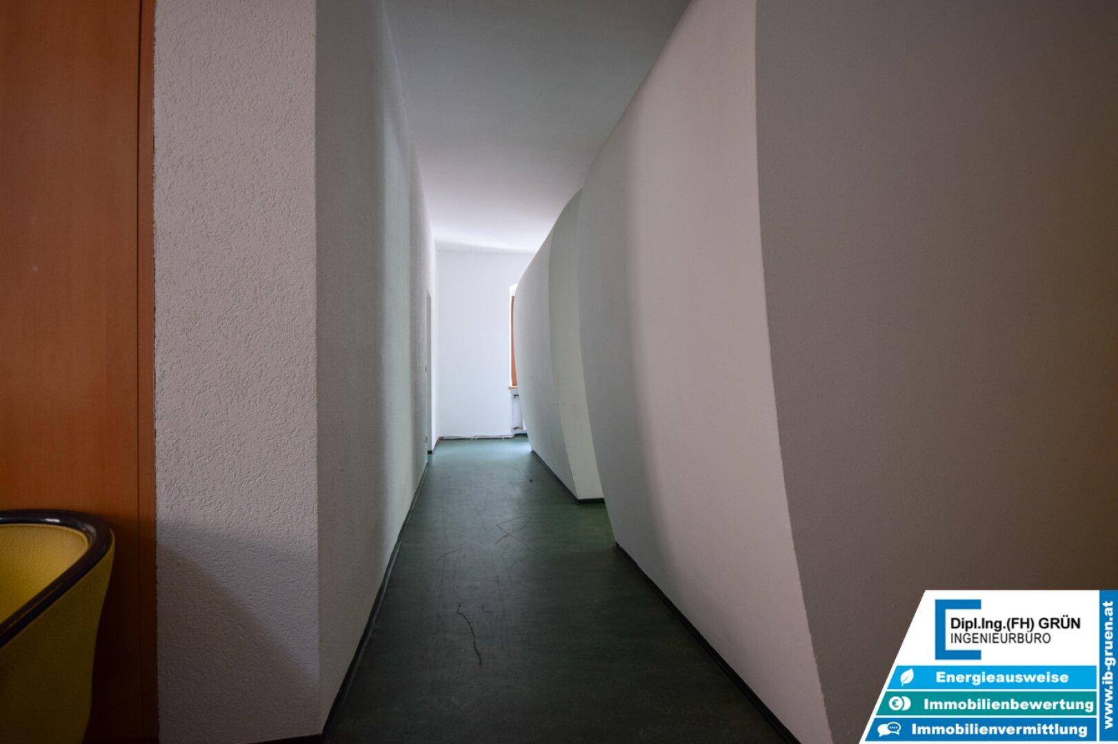 Langer, schmaler Flur mit geschwungenen Wänden und dunklem Bodenbelag.