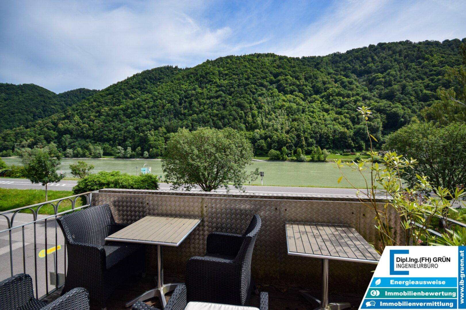 Balkon mit Sitzgelegenheiten und weitem Blick auf den Fluss und bewaldete Berge.