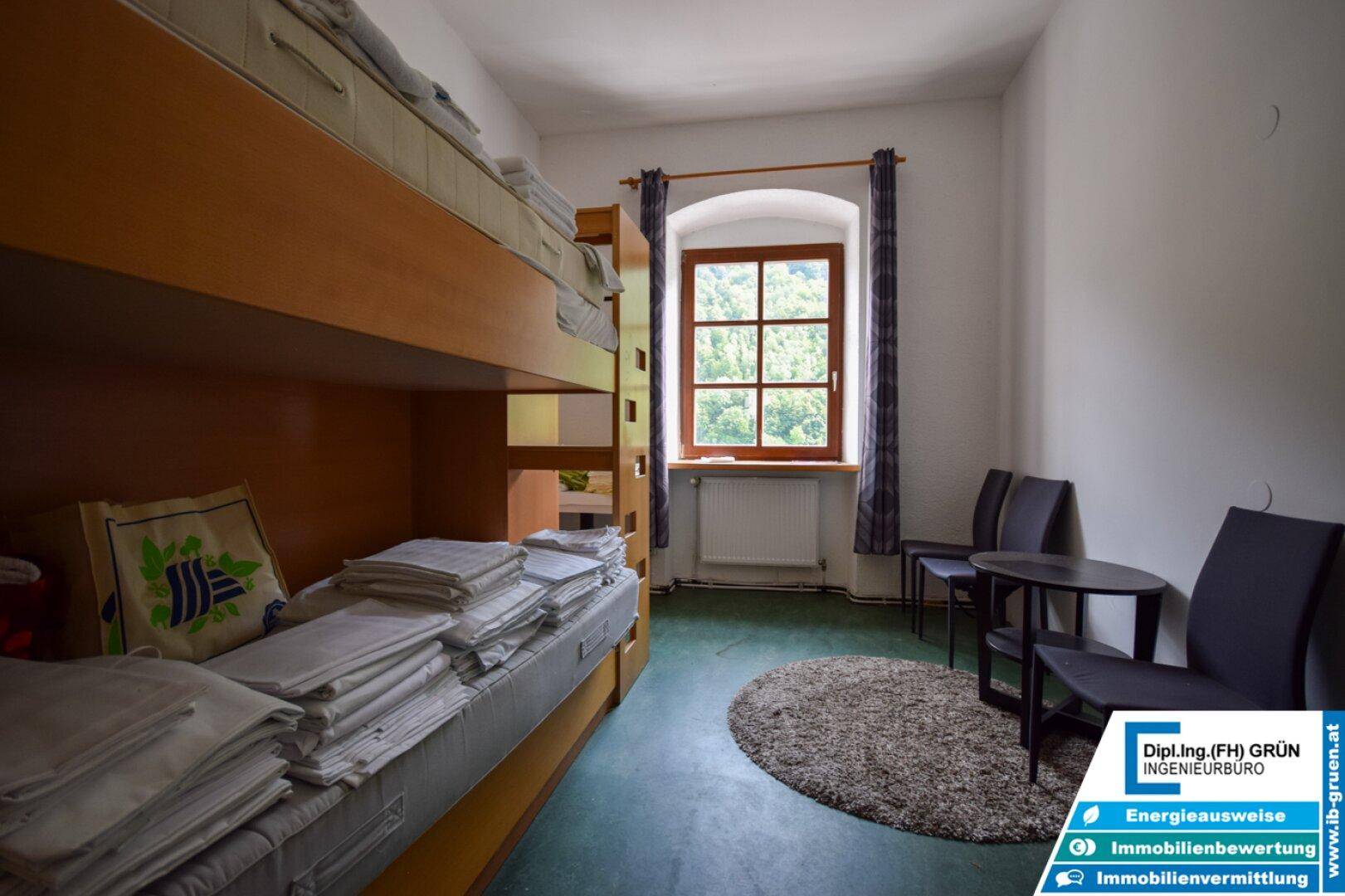Schlafzimmer mit Etagenbett, kleinem Tisch und Stühlen, sowie Fenster.