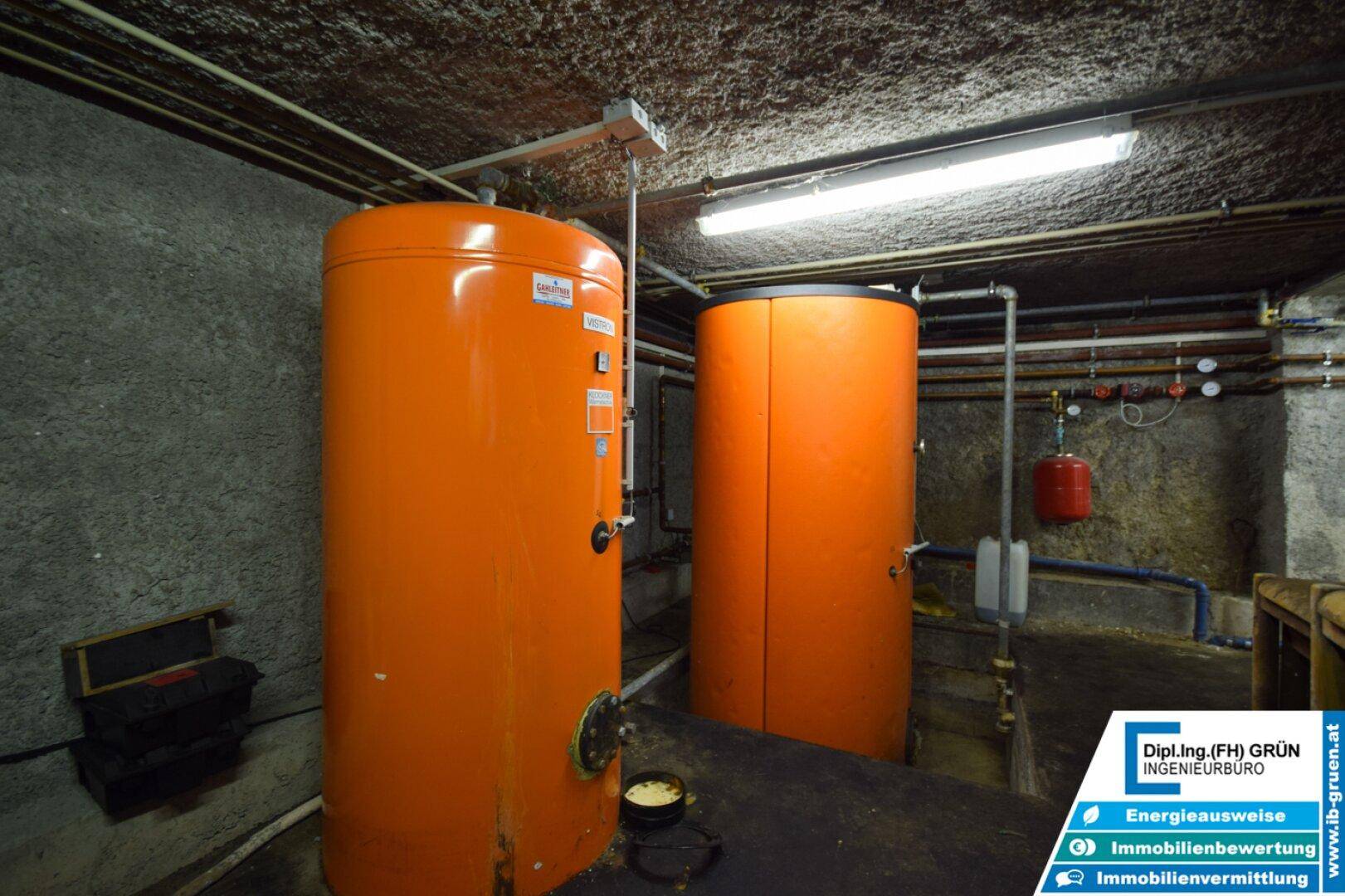 Heizungsraum mit zwei großen orangefarbenen Warmwasserspeichern und Rohrleitungen.
