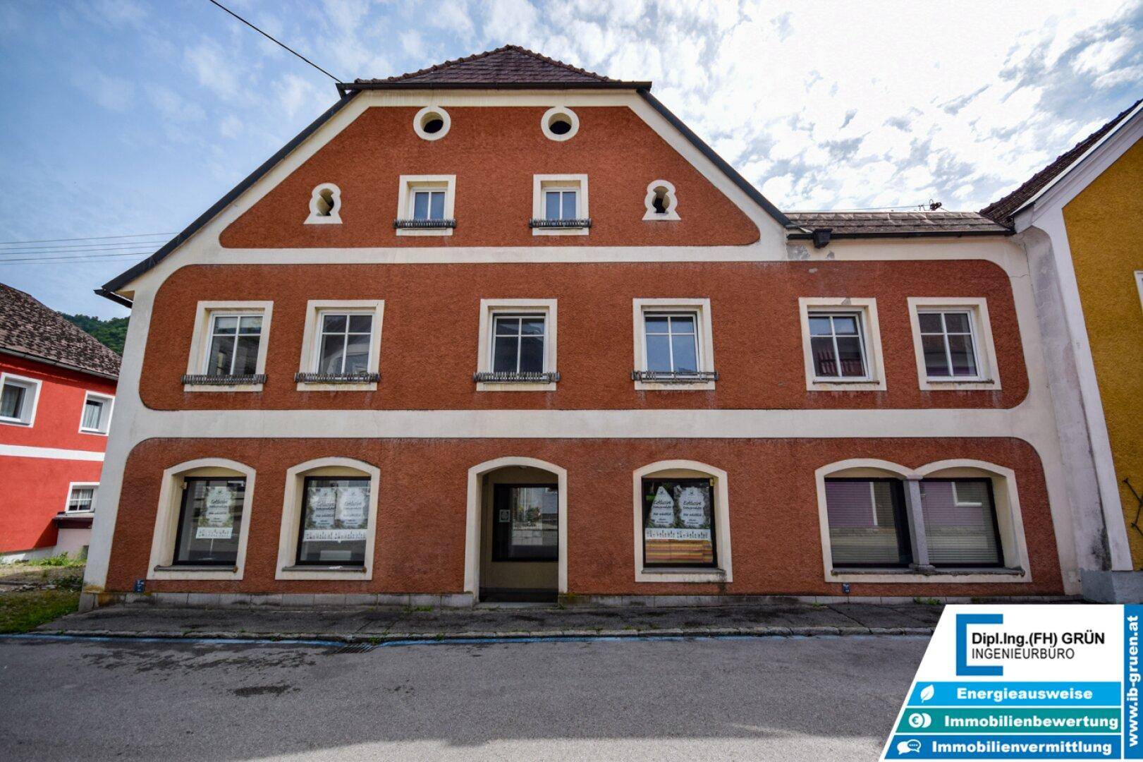 Vorderansicht eines historischen Gebäudes mit roter Fassade und mehreren Fenstern.